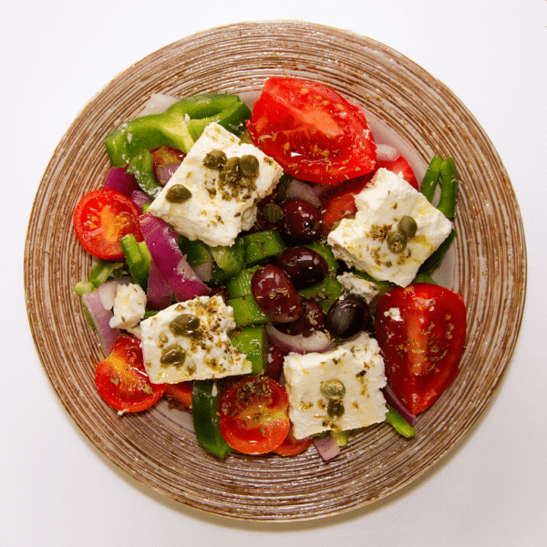 Salade avec des tomates, des poivrons, des olives et de la féta joliment posé dans une assiette